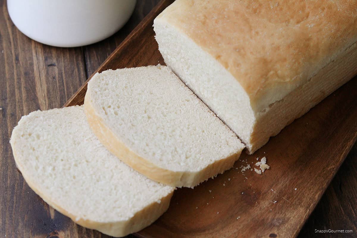 loaf and slices of white sandwich bread on wood tray